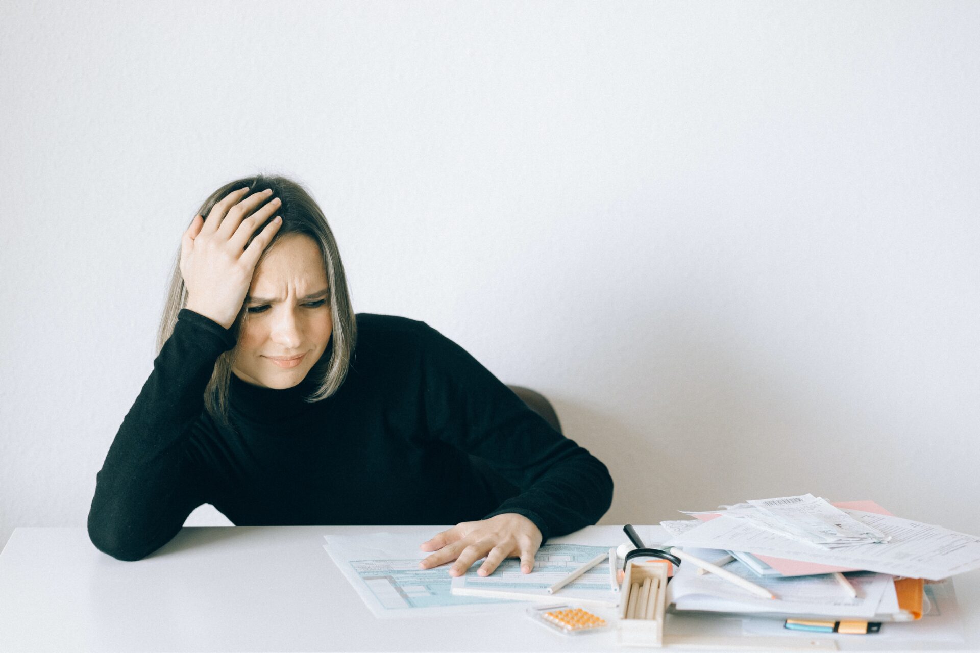 Woman with hand on head near pile of paper on desk (Photo by Nataliya Vaitkevich from Pexels)