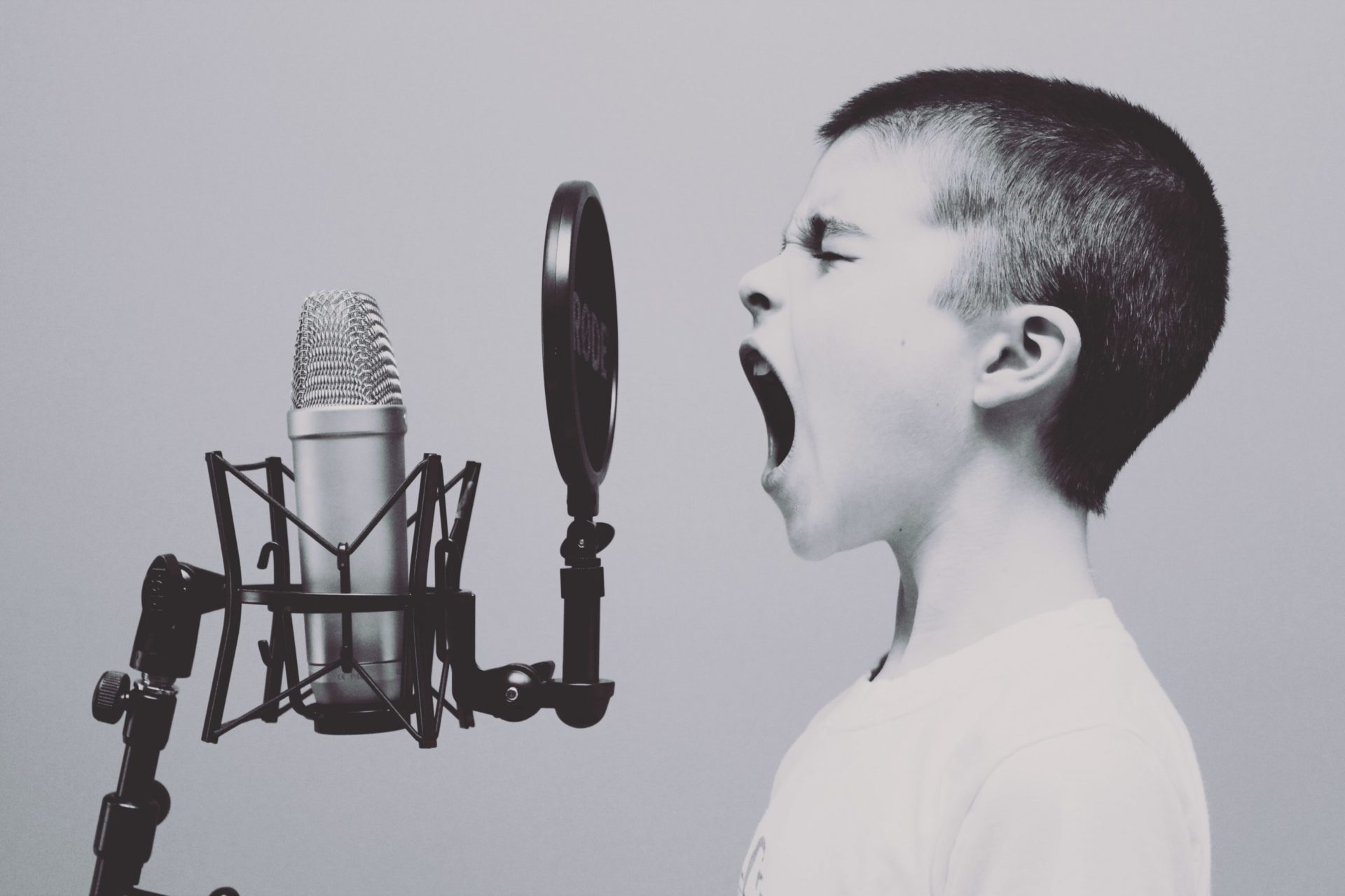 Boy singing into microphone with pop filter. (Photo by Jason Rosewell on Unsplash)