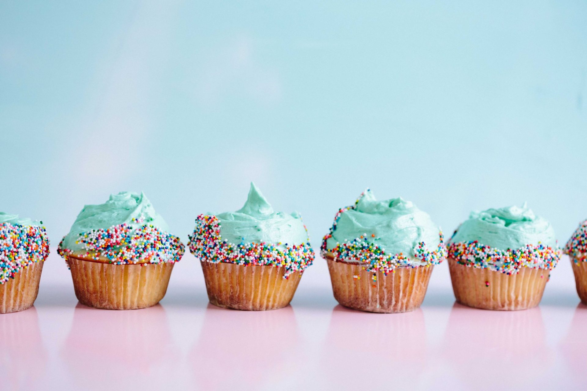 Six teal-coloured icing cupcakes with sprinkles in a row. (Photo by Brooke Lark on Unsplash)