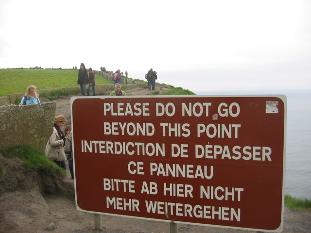 A warning sign at the Cliffs of Moher being ignored by walkers choosing to follow a dangerous cliff path
