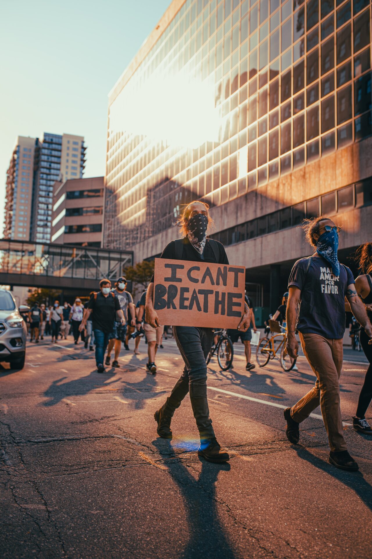 People wearing masks march in protest. One holds a sign reading "I can't breathe" (Photo by Josh Hild on Unsplash)